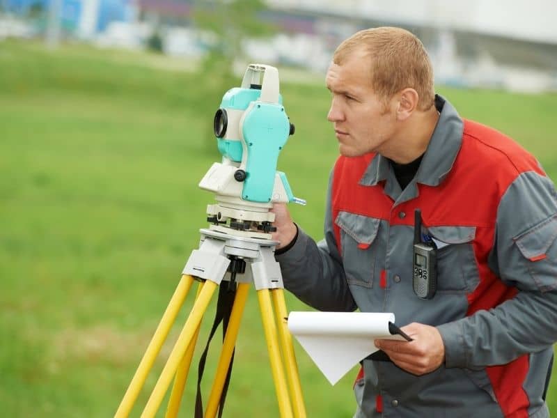 Surveyor verifying finished lot conditions with boundary surveying equipment before builder turnover and closing.
