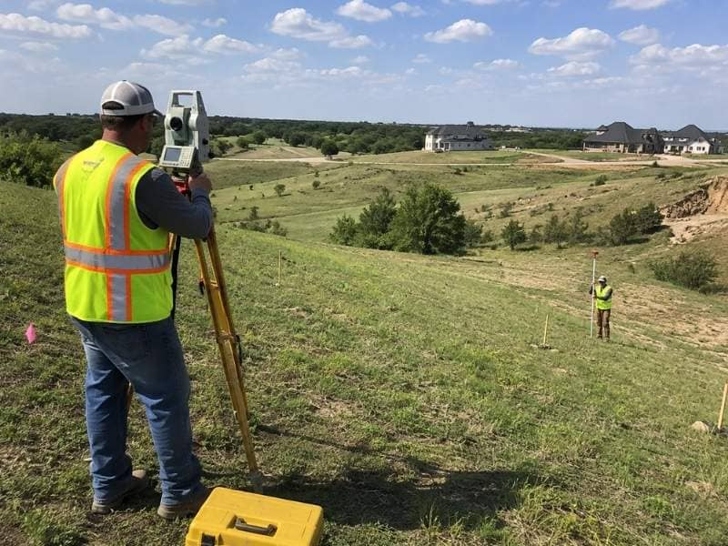 Topographic surveyor measuring elevations on a sloped residential property in McKinney Texas