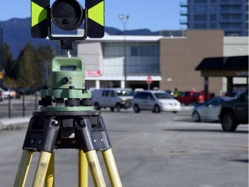 ALTA Land Title Survey Commercial Property McKinney Texas - Mckinney Land Surveying Surveying instrument mounted on a tripod in a parking lot with a building in the background, ready for measurement work.